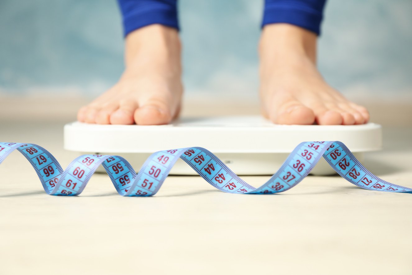 Person's Feet Standing on Weighing Scale with Tape Measure